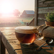 Glass mug with a layered mushroom coffee on a wooden table, barn in the background