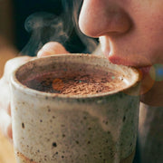Person drinking cacao from a steaming mug with a blurred background