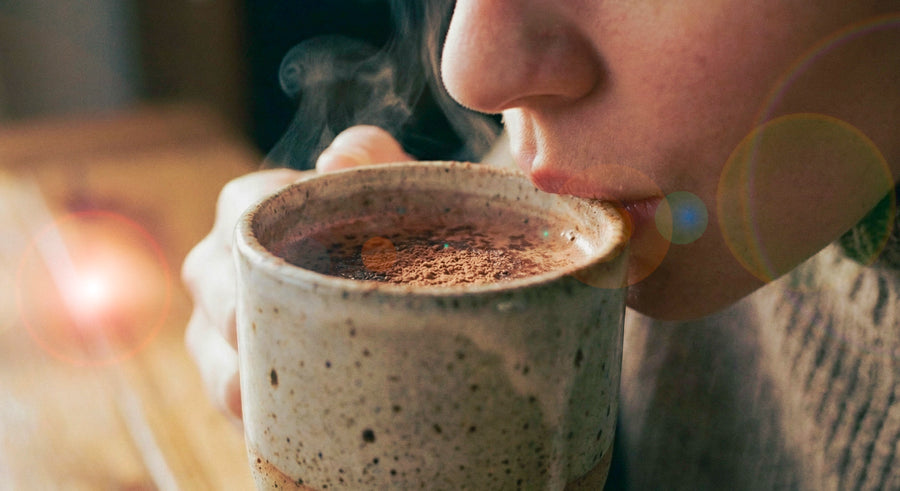 Person drinking cacao from a steaming mug with a blurred background