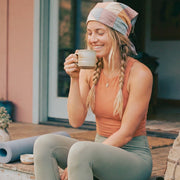 Woman sitting on a porch holding a mug, wearing a headband and tank top.